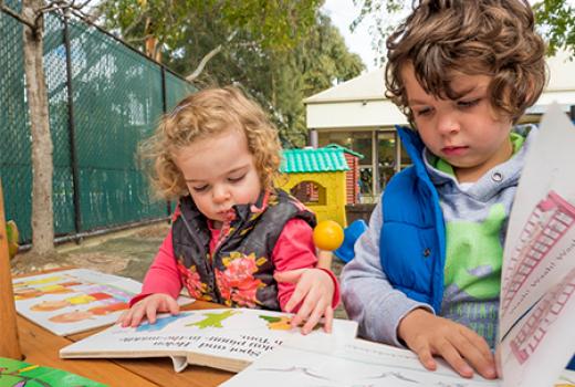 Two young children looking at books at a table in a playground